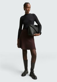 Zwarte geribde lange mouw top, maroon uitlopende rok, zwarte kniehoge laarzen met dikke zolen en een grote zwarte handtas.