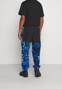 Camiseta negra y pantalones deportivos con un patrón abstracto en azul y negro, fabricados en material suave, con una cinturilla elástica y puños ajustados.
