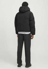 Schwarze Steppjacke mit Kapuze, gesteppter Textur und elastischen Bündchen, kombiniert mit dunkler Hose und robusten schwarzen Schuhen.