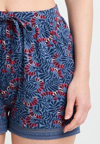 Shorts en coton à motifs avec un fond bleu, ornés de designs floraux rouges et roses. Taille avec cordon de serrage et ourlet détaillé.