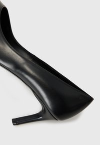 Scarpa nera in pelle con tacco alto, punta affusolata e sottile tacco a stiletto. Presenta un logo discreto sul lato. Texture liscia.