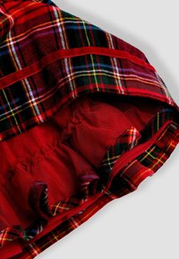 Raudona plaid medžiaga su žaliais, geltonais ir mėlynais akcentais; turi raustu raudoną pamušalą ir glotnų paviršių. Parodo drabužio vidaus detales.