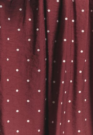 Tessuto bordeaux con una finitura texture, caratterizzato da pois bianchi distribuiti uniformemente, creando un motivo semplice ma distintivo.