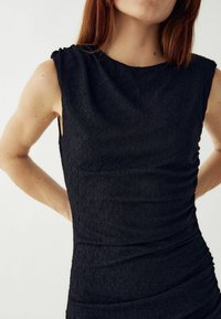 Čierne šatové šaty bez rukávov s textúrovaným vzorom, priliehavým strihom a nariasenými detailmi po stranách. Mäkka tkanina s hladkým povrchom.