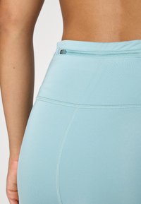 Lyse blå leggings har en høy midje med en glidelåslomme. Stoffet har en glatt tekstur og pent søm langs sømmene.