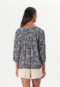 Navy og hvit mønstrete bluse med trekvart ermer, rund hals, og rynkede detaljer på baksiden, sammen med beige shorts.