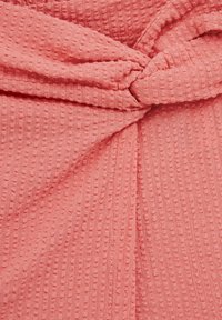 Koraļļu tekstūrēta auduma ar nelielu režģa rakstu, centrā ar sasietu mezglu detaļu, mīksta un plūstoša izskata.