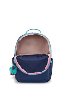 Mochila azul marino con ribete aqua, compartimento principal abierto mostrando el interior beige, y un pequeño llavero de mono de peluche azul adjunto.