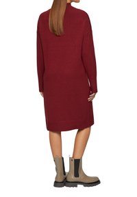 Burgunderfarbendes Strickkleid mit langen Ärmeln und lockerem Schnitt, kombiniert mit grauen Knöchelstiefeln mit schwarzen elastischen Seiteneinsätzen.