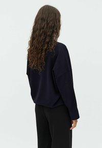 Navy knitted sweater with a relaxed fit, dropped shoulders, and long sleeves, paired with black trousers, showcased from the back.