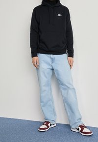 Svart huvtröja med frontficka, ljusblå raka jeans och burgunder/vita sneakers med svarta detaljer.