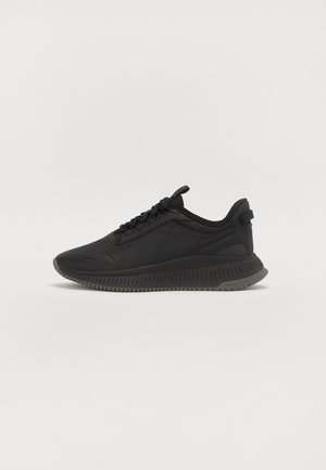 Sort atletiksneaker med tekstureret overdel, snørelukning, trækstrop ved hælen og tyk mønstret sål på en ensartet lys baggrund.