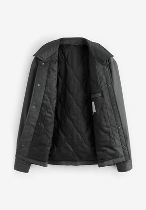 Die graue Steppjacke hat ein glattes, dunkles Futter mit einem Diamantmuster. Der Kragen und die Bündchen haben eine strukturierte Oberfläche. Die Knopfverschlüsse sind sichtbar.