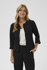 Giacca nera con tessuto strutturato, rifinitura arricciata e due tasche frontali. Indossata sopra una camicetta chiara, abbinata a pantaloni neri.