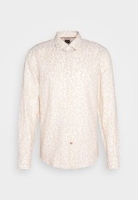 Chemise beige à manches longues avec boutons, motif subtil de feuilles blanches et col pointu, présentée sur un fond gris uni.