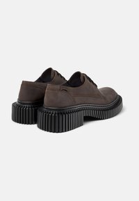 Brune snørebåndssko med en distinkt tyk gummisål med ribbet design. Skoene ses fra bagenden, hvilket fremhæver deres form.