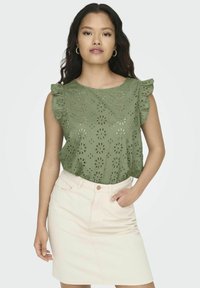 Zielona bluzka z haftem kwiatowym i falbaniastymi rękawami, zestawiona z jasnym dżinsowym spódnicą. Materiał wydaje się lekki i ma miękką teksturę.