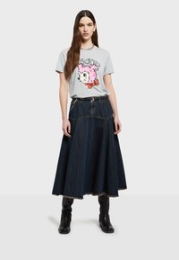 Camiseta gráfica gris con un personaje de dibujos animados rosa. Combinada con una falda larga de mezclilla oscura, detallada con un dobladillo deshilachado y una cremallera lateral.