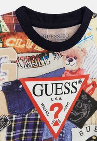 Sweatshirt graphique coloré présentant un mélange de motifs en tissu. Les couleurs principales incluent le bleu, le rouge et le jaune avec un logo triangulaire proéminent.