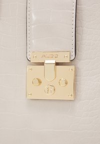 Light beige crocodile-embossed leather handbag with a shiny gold rectangular clasp engraved with "ALDO."