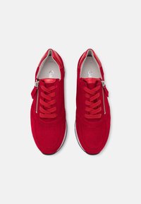 Zapatillas de gamuza roja con diseño perforado, punta redonda, acentos en contraste, cordones planos y cierre lateral con cremallera. Detalle de hardware en plata.