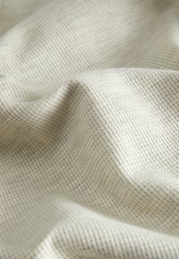 Woven fabric with a soft, textured surface in light cream color; features a grid pattern and gentle draping, showing subtle depth and dimension.