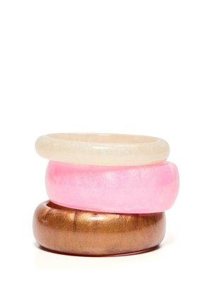 Három egymásra rakott, fényes gyanta karkötő bézs, rózsaszín és fémes bronz színben fehér háttéren.