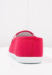 Červené plátěné slip-on boty s bílou gumovou podešví, které mají strukturovaný svršek a hladký, kulatý podpatek. Bez viditelného brandingu nebo ozdob.