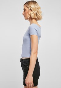 Top scurt cu mânecă scurtă de culoare bleu deschis, cu un design ajustat, decolteu rotund și lungime scurtă, asortat cu pantaloni scurți negri cu talie înaltă.