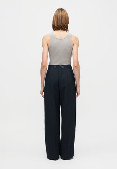 Grijs geribd tanktop met zwarte wijde broek met een getailleerde pasvorm en taillebanddetails, gezien van achteren.