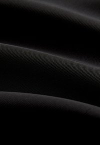 Gros plan sur un tissu noir lisse avec une texture subtile en côtes diagonales et des plis doux créant de légères ombres.