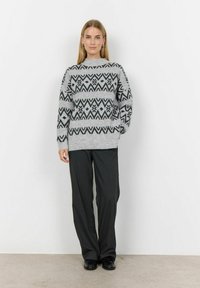 Grijze gebreide trui met een geometrisch zwart patroon, ronde halslijn en een losse pasvorm, gecombineerd met zwarte broek en glanzende zwarte schoenen.