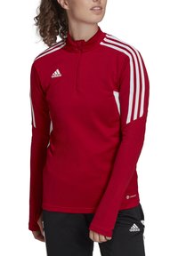 Rood sportief langmouwtop met een halve rits, witte zijstrepen en ribbelstructuur. Voorzien van het Adidas-logo op de borst en onderrand.