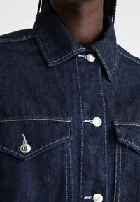 Dark denim shirt featuring a classic collar, silver button closures, and two chest pockets with contrasting stitching details.