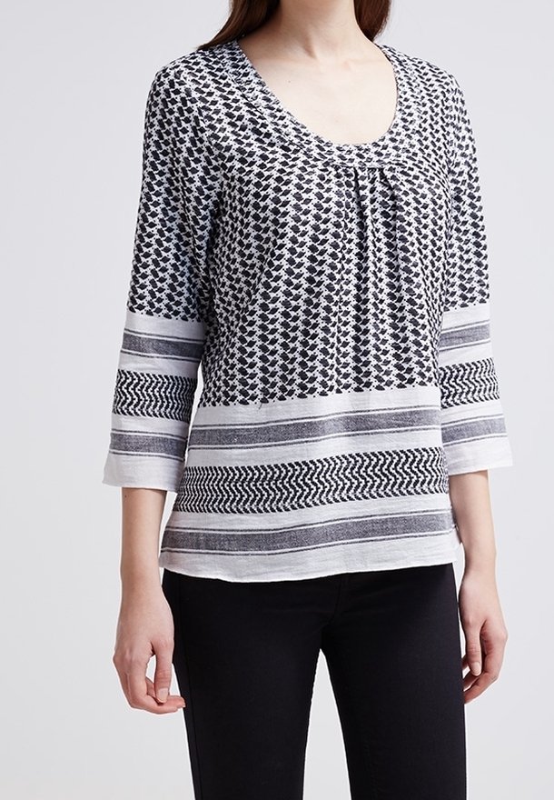 Femme portant un haut à manches trois-quarts noir et blanc avec des rayures et des motifs géométriques, associé à un pantalon noir ajusté.