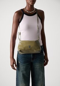Grønn lærveske med teksturert overflate, med en sølvkjedestropp og en liten logo på forsiden. Bært med denimjeans.