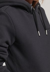 Felpa nera in cotone con tasca a marsupio, coulisse e dettagli argentati. Tessuto morbido e polsini a coste, con ricamo del logo del marchio.