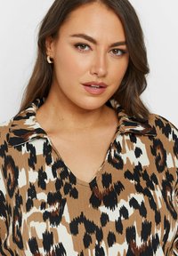 Blusa marrone e crema con un motivo a stampa leopardata, dotata di scollatura a V e ampio colletto, realizzata in un tessuto strutturato.