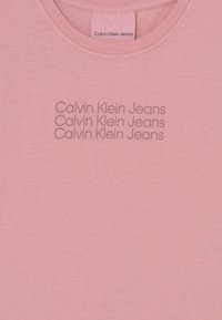Różowy bawełniany t-shirt z okrągłym dekoltem, z powtarzającym się na przodzie napisem "Calvin Klein Jeans" w jaśniejszym odcieniu różu.