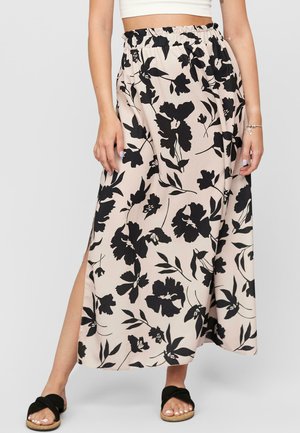 Floral maxi skirt in beige with black flower patterns. Features a smocked waist and a side slit. Paired with black flat sandals.