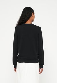 Čierna mikina s dlhými rukávmi, okrúhlym výstrihom a rebrovanými manžetami. Vyrobená z mäkkej látky, s hladkým povrchom a voľným strihom.