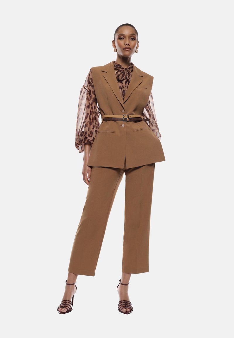 Completo marrone su misura con rever appuntiti, pantaloni a vita alta e vita con cintura. La blusa presenta una stampa leopardata con maniche a sbuffo trasparenti.