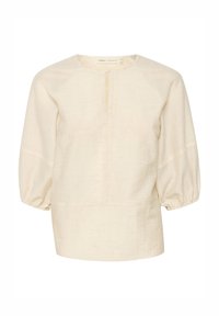 Blouse beige à manches longues avec col rond, pli subtil sur le devant et manches légèrement bouffantes rassemblées aux poignets.