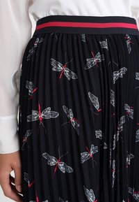 Zwarte geplooide rok met een rood en marineblauw gestreepte tailleband, versierd met witte en rode motillustraties over de hele stof.