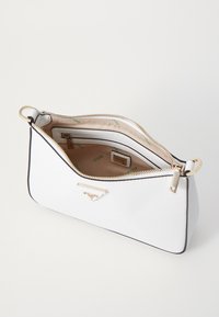 Sac zippé blanc avec surface texturée, matériel en or et intérieur beige comportant un logo et plusieurs poches.
