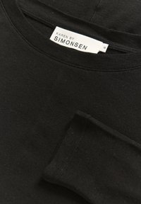 Zwarte katoenen blouse met lange mouwen en een ronde halslijn. Voorzien van een label met de tekst "KAREN BY SIMONSEN." Soepele textuur met subtiele stikseldetails.