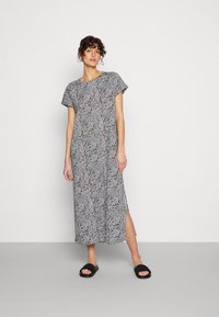 Vestido maxi com padrão de folhas em preto e branco com detalhes em verde, mangas curtas, fendas laterais e uma silhueta relaxada e reta.