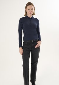 Granatowa koszulka polo z długim rękawem, ozdobiona plisą i guzikami, w połączeniu z czarnymi jeansami o prostych nogawkach. Minimalistyczny design i średniej grubości tkanina.