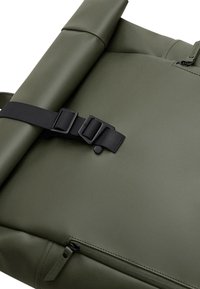 Olive green roll-top backpack made of durable material, featuring a black buckle strap, zipper closure, and a textured finish.