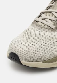 Leichte Sportschuhe mit einem atmungsaktiven Mesh-Obermaterial in sanftem Beige, strukturiertem Zehenbereich und schwarzer Gummisohle.